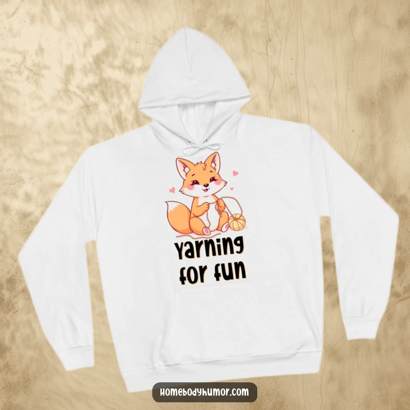 Happy fox playfully crafting with yarn hoodie, a warm and humorous top for creative individuals.